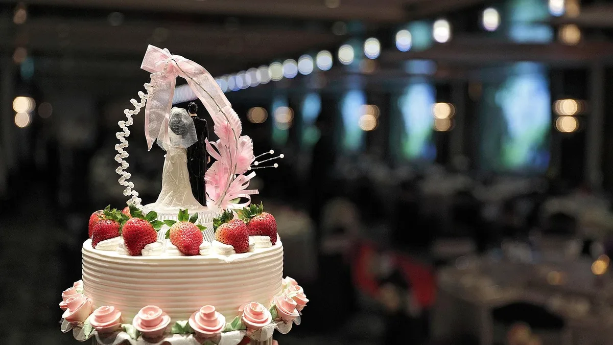 A wedding cake with a bride and groom figurine on top, surrounded by strawberries and flowers.
